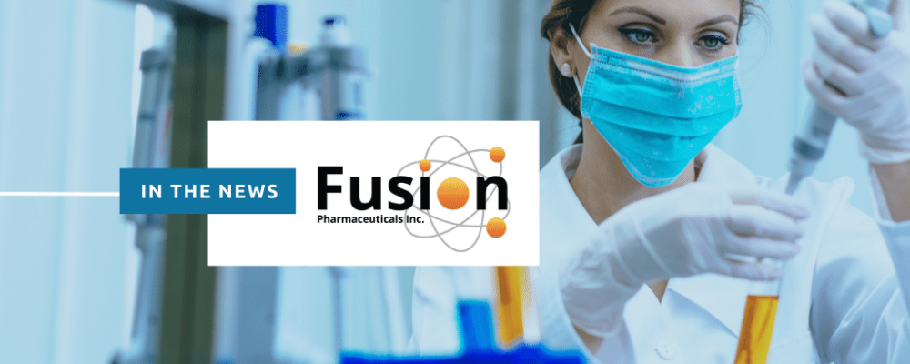 In the news: Fusion Pharmaceuticals. The background image is a woman researcher working in a lab while wearing personal protective equipment (PPE).